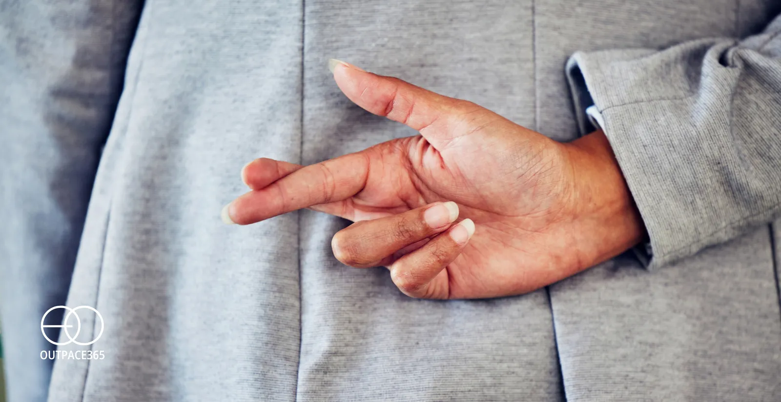A man in a suit holding his fingers crossed behind his back