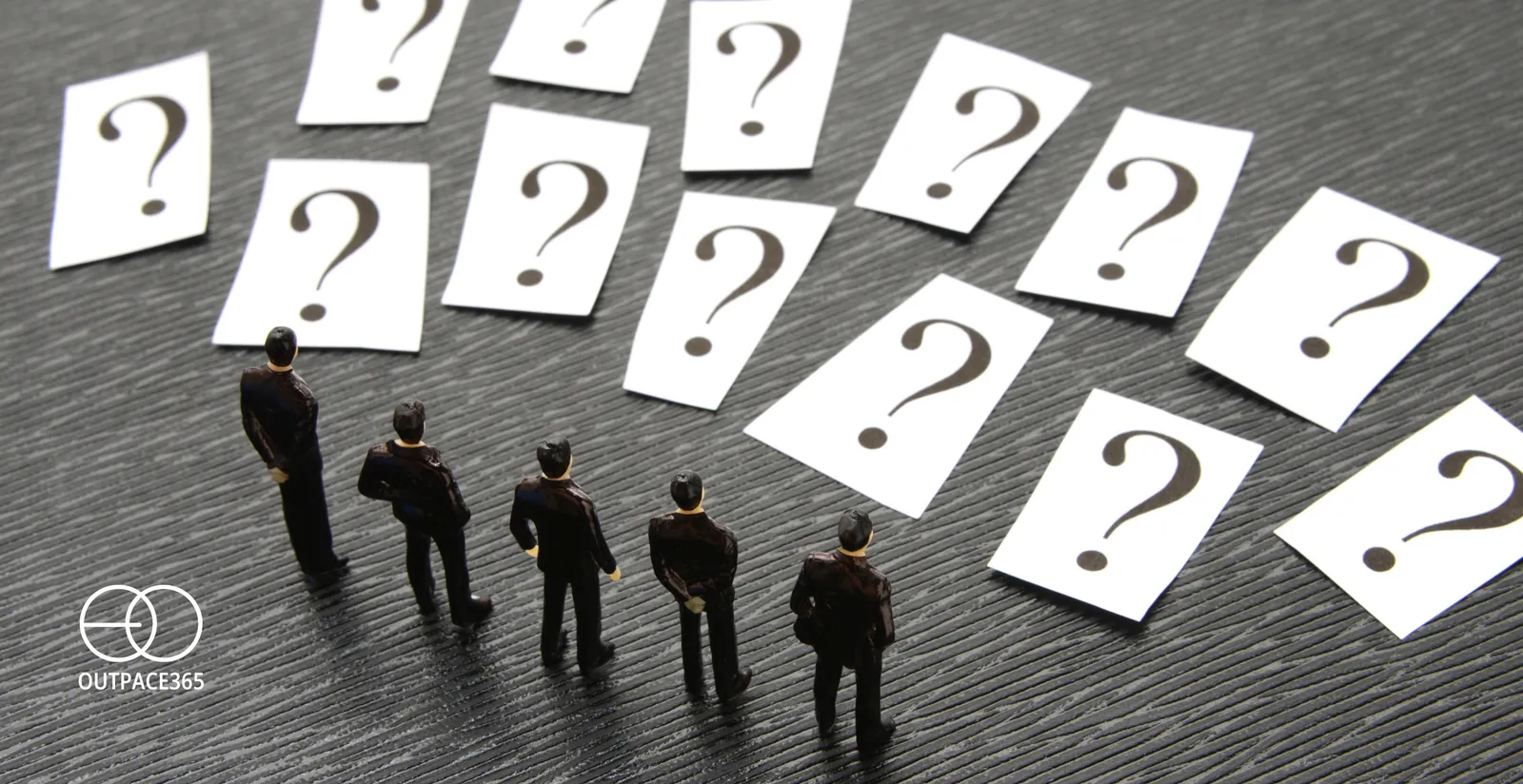 Miniature figures facing a wall of question-mark cards