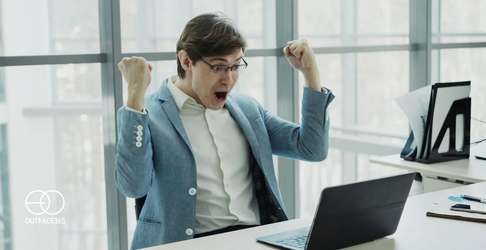A man at an office desk celebrating with both fists raised