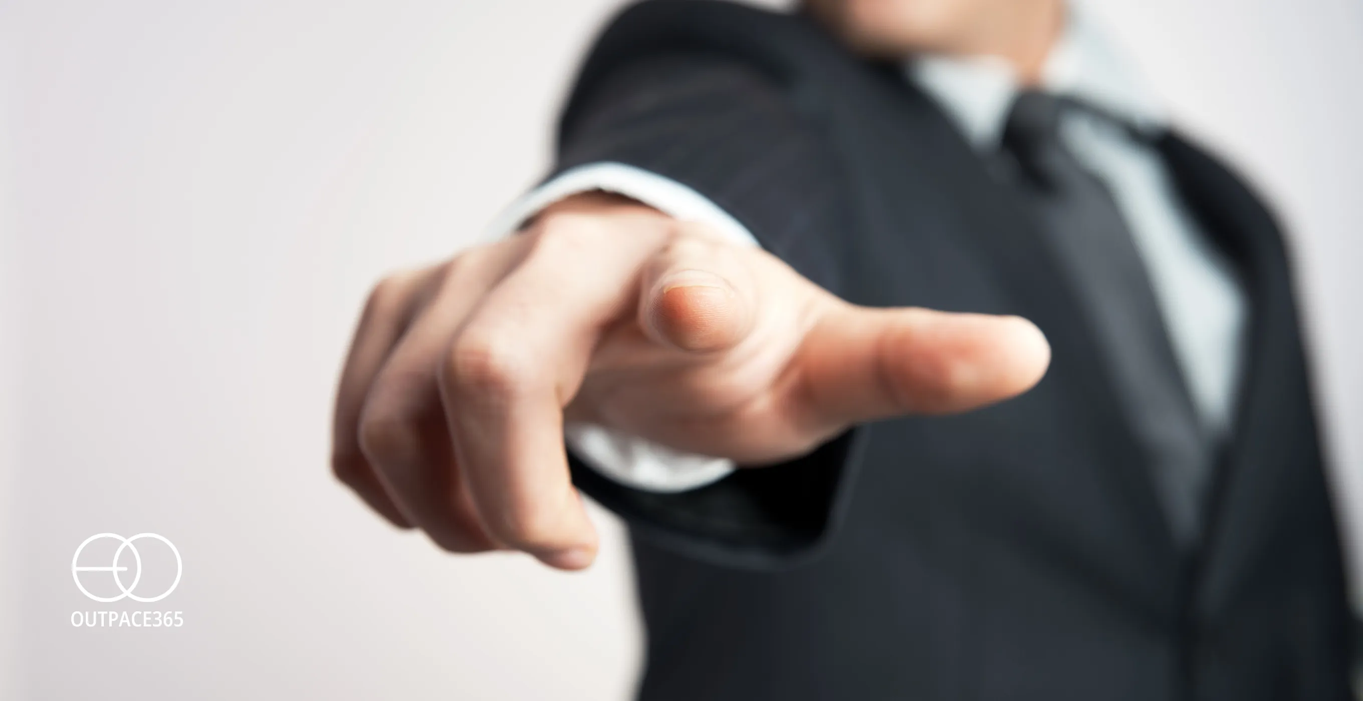 A close-up of a man in a suit pointing towards the viewer