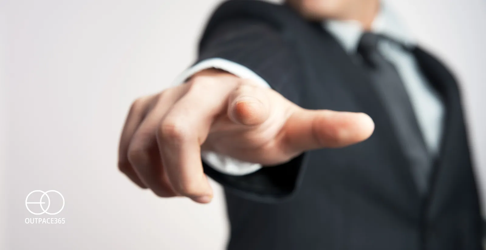 A close-up of a man in a suit pointing towards the viewer